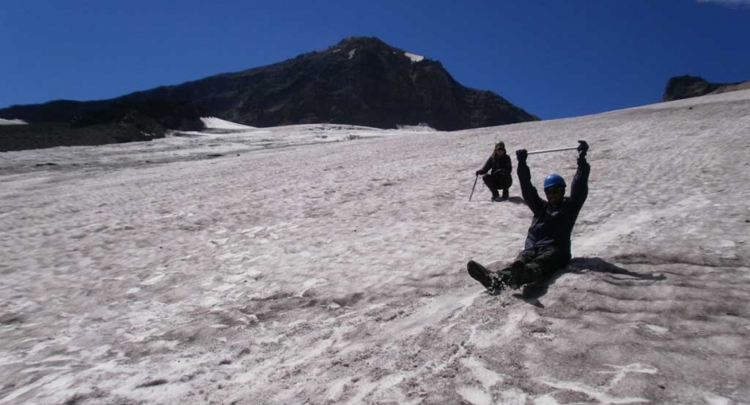 a person raises their hands as they sit and slide down a snowy slope
